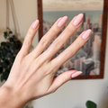 Hand with almond-shaped nails painted in KAG - Gel neutral peachy pink gel polish against blurred cityscape background thumbnail