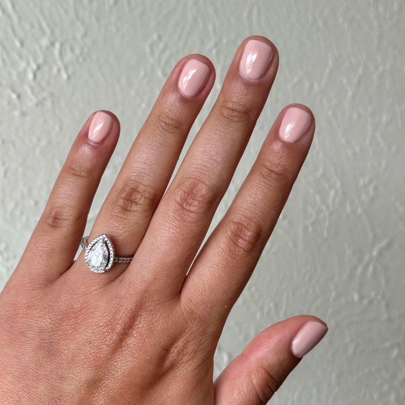 Hand with short oval nails painted in KAG - Gel neutral peachy pink gel polish against light textured wall background