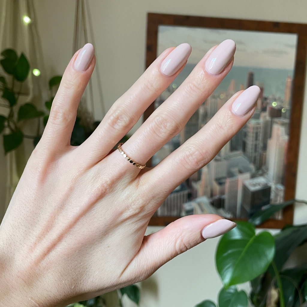 Hand with oval nails polished in Kitten neutral grey beige for a smooth, elegant mani look against indoor background