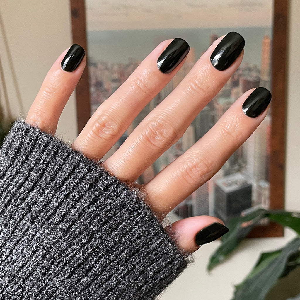 Hand with glossy Latenight quick dry polish manicure on natural nails wearing cozy gray sweater against blurred city view