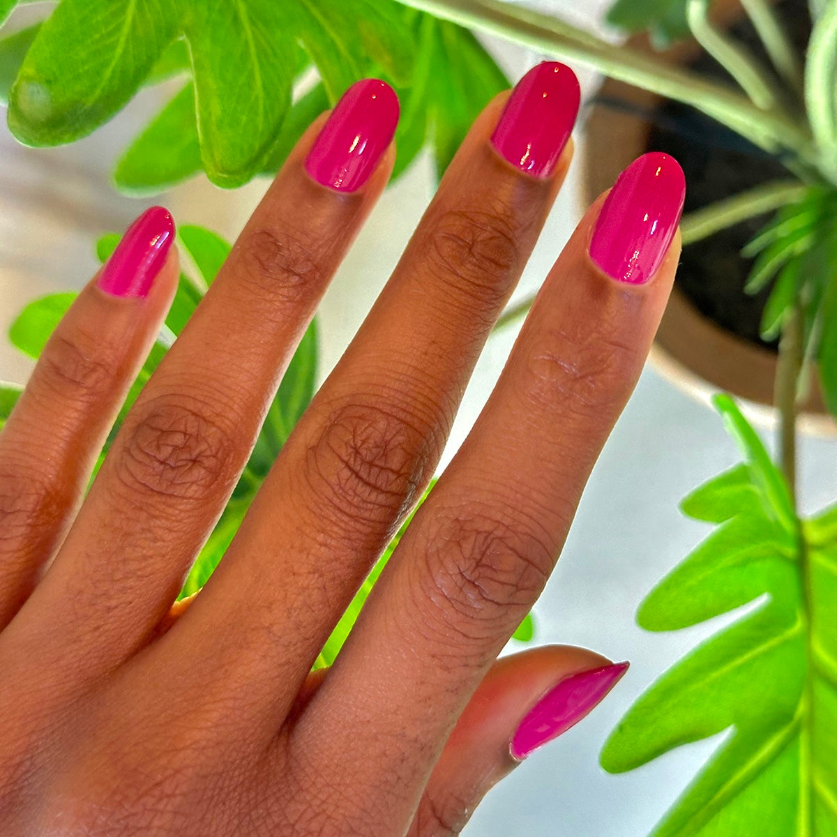 Hand with glossy Leotard quick dry gel polish manicure on medium-length nails against green plant background