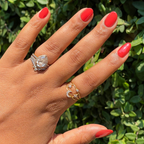 Hand with glossy bright orange-red Let’s Circle Back gel polish manicure shown outdoors against green leaves background