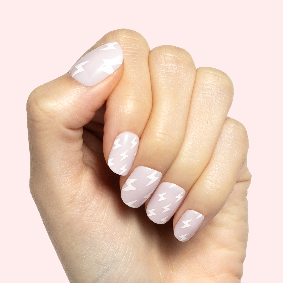 Lightning Strike | Extra Short | Squoval - Tab Press-On neutral false nails with white lightning bolt pattern on hand against pale pink background