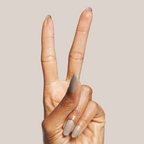 Hand with almond shaped nails in sheer grey Moonlit gel polish holding two fingers up on neutral background