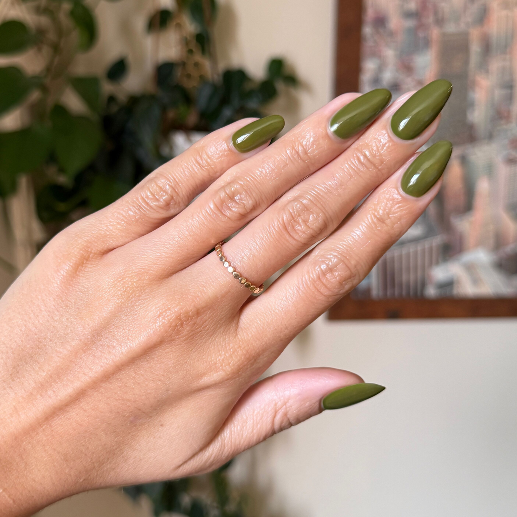 Hand with long nails painted in Mossy gel polish showing glossy quick dry manicure with delicate gold ring