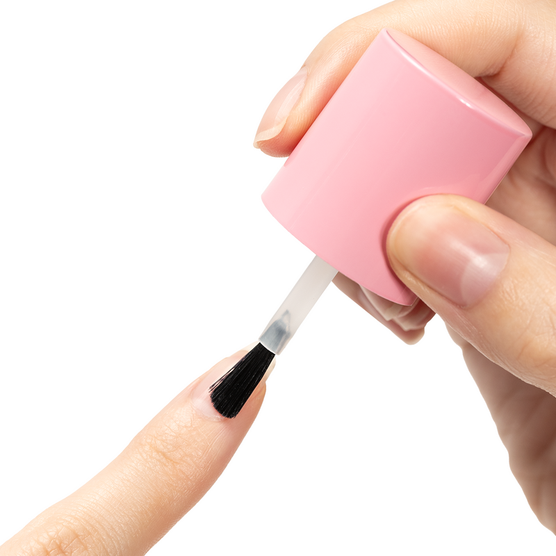 Nail Hardener being brushed on natural nail for strengthening and protection during at-home manicure care.