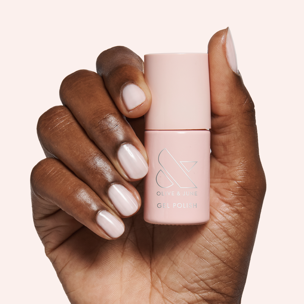 Hand holding Dream Job - Gel polish bottle with neutral milky sheer pink gel manicure on pale background