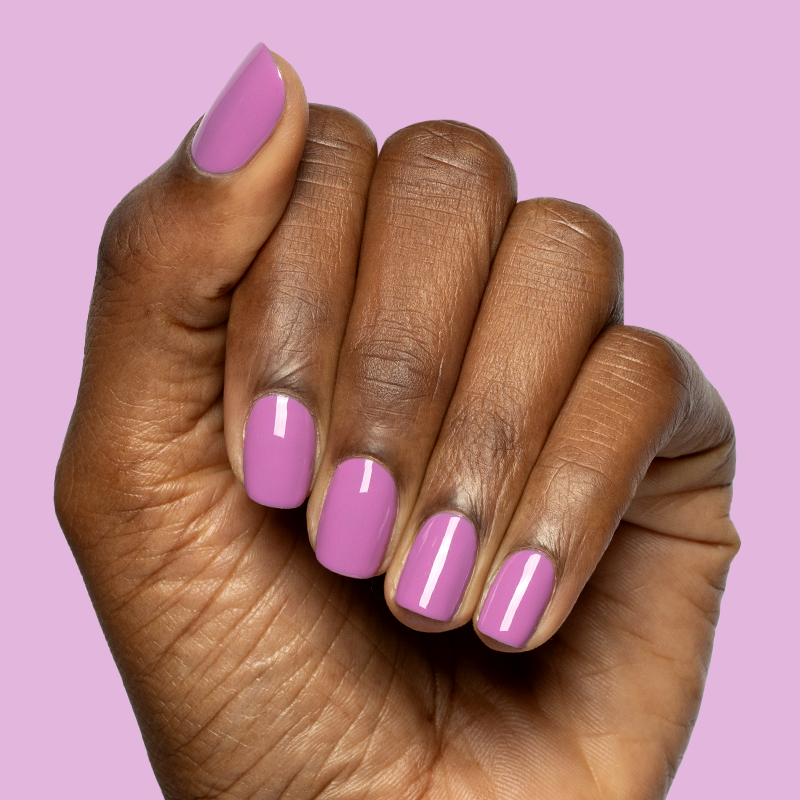 Hand with nails painted in bright floral purple pink shade using Petal - Gel polish on soft purple background