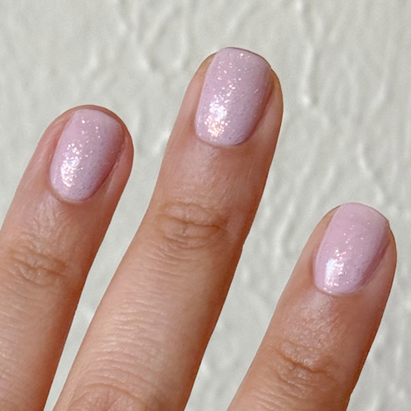 The Pixie Effect Top Coat adding subtle iridescent shimmer over light pink polish for a delicate manicure finish
