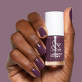 Hand with short nails painted in Plum gel polish holding Olive and June quick dry nail polish bottle against matching background