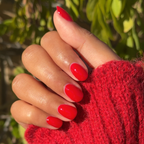Hand with oval nails painted in olive and June Secret Recipe nail polish against green outdoor background