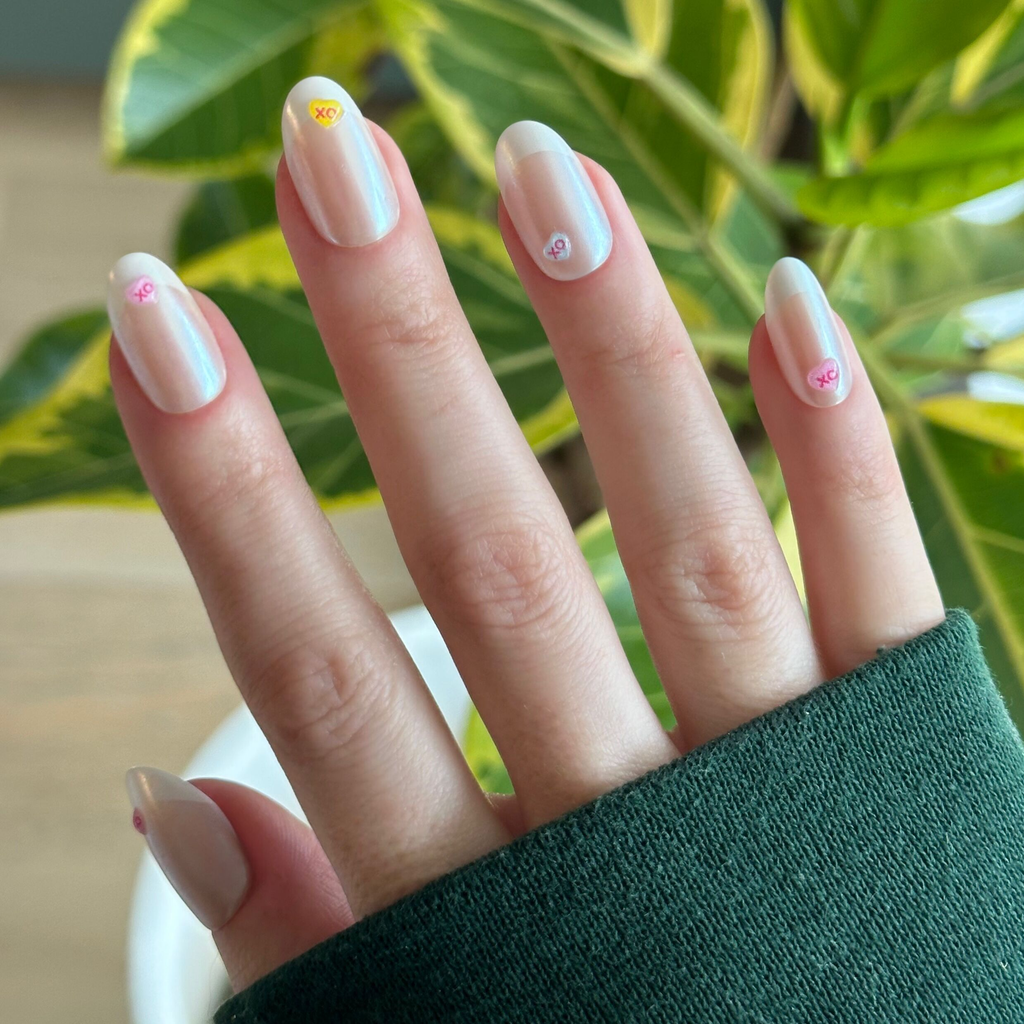 Hand wearing Puffy Chrome Candy Heart French - Press On | Medium | Oval nails with 3D candy heart details outdoors near green leaves