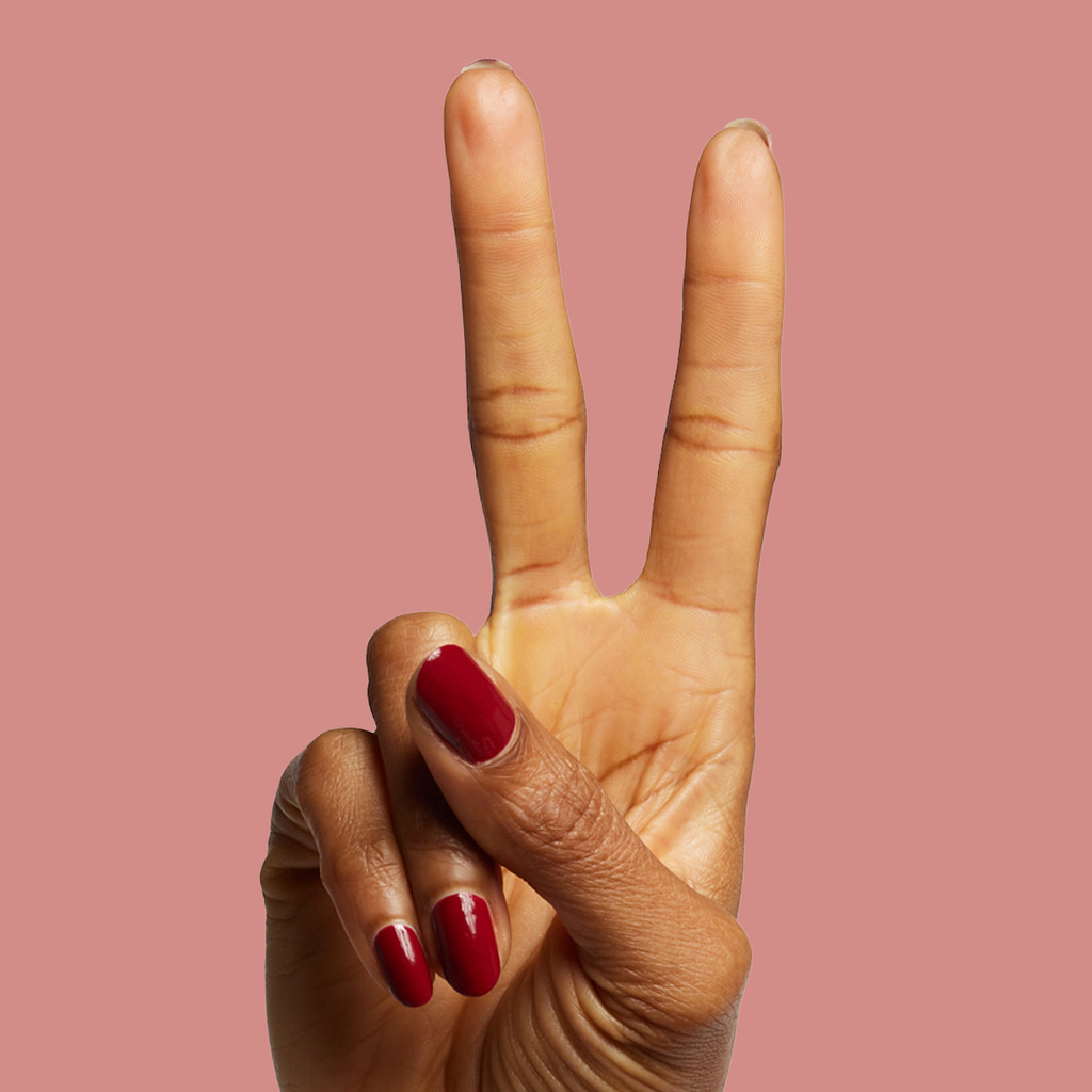 Hand showing glossy deep red manicure with Brick polish on medium skin against a warm muted background