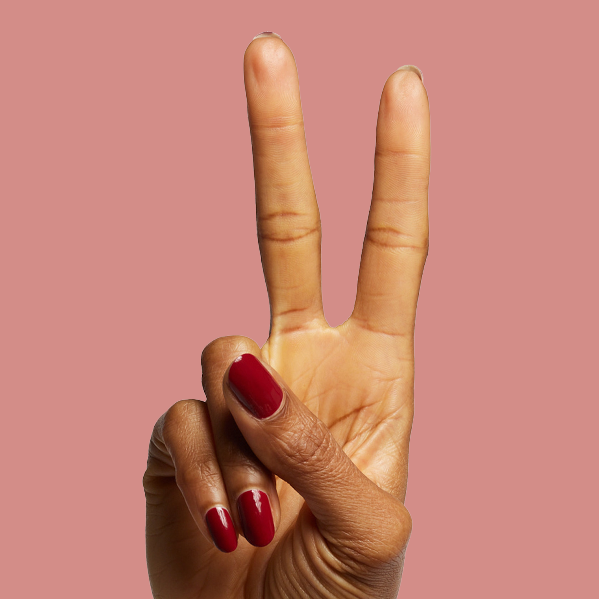 Hand showing glossy deep red manicure with Brick polish on medium skin against a warm muted background