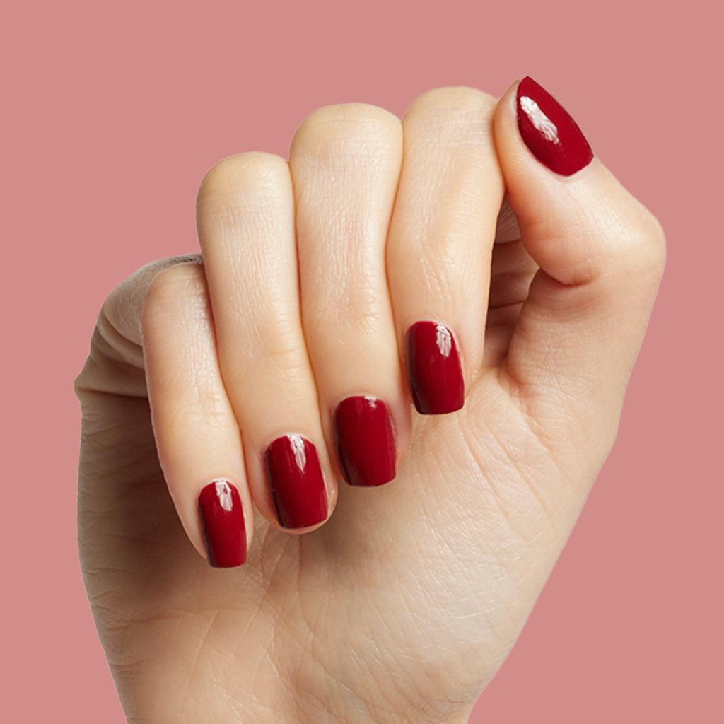 Hand showing glossy deep red manicure with Brick polish against a muted pink background for an at-home mani