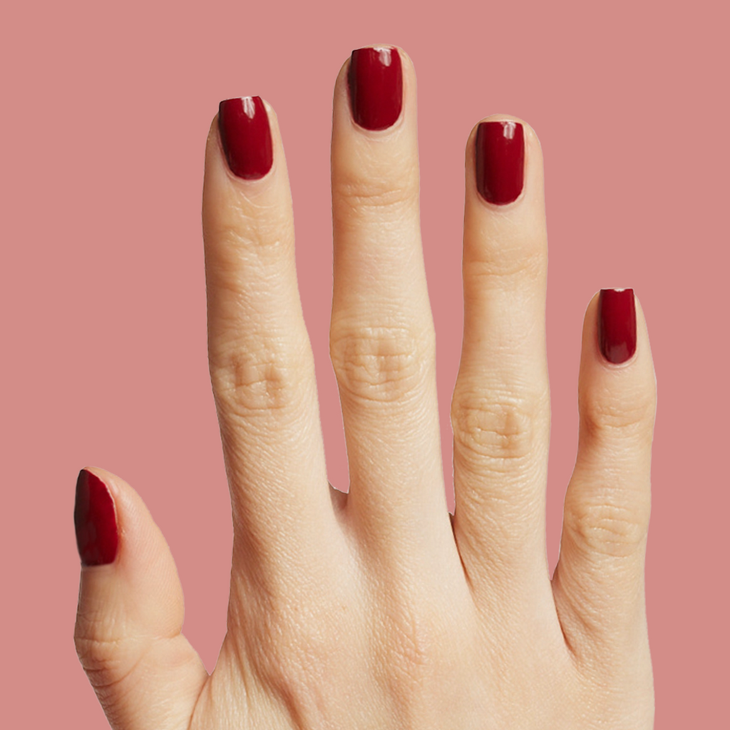 Hand with Brick polish showing rich deep red manicure on natural skin against a soft muted pink background