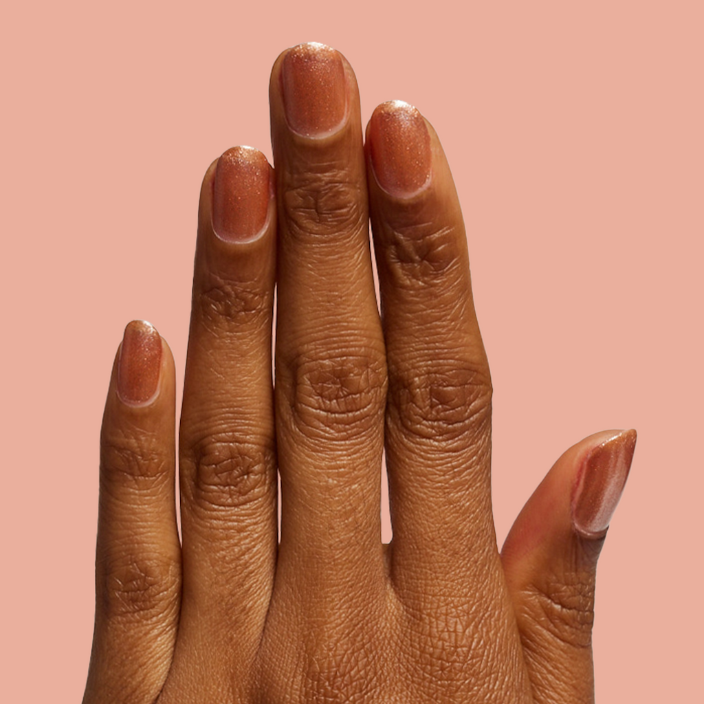 Hand with Penny polish showing shiny copper metallic manicure on medium skin against peach background