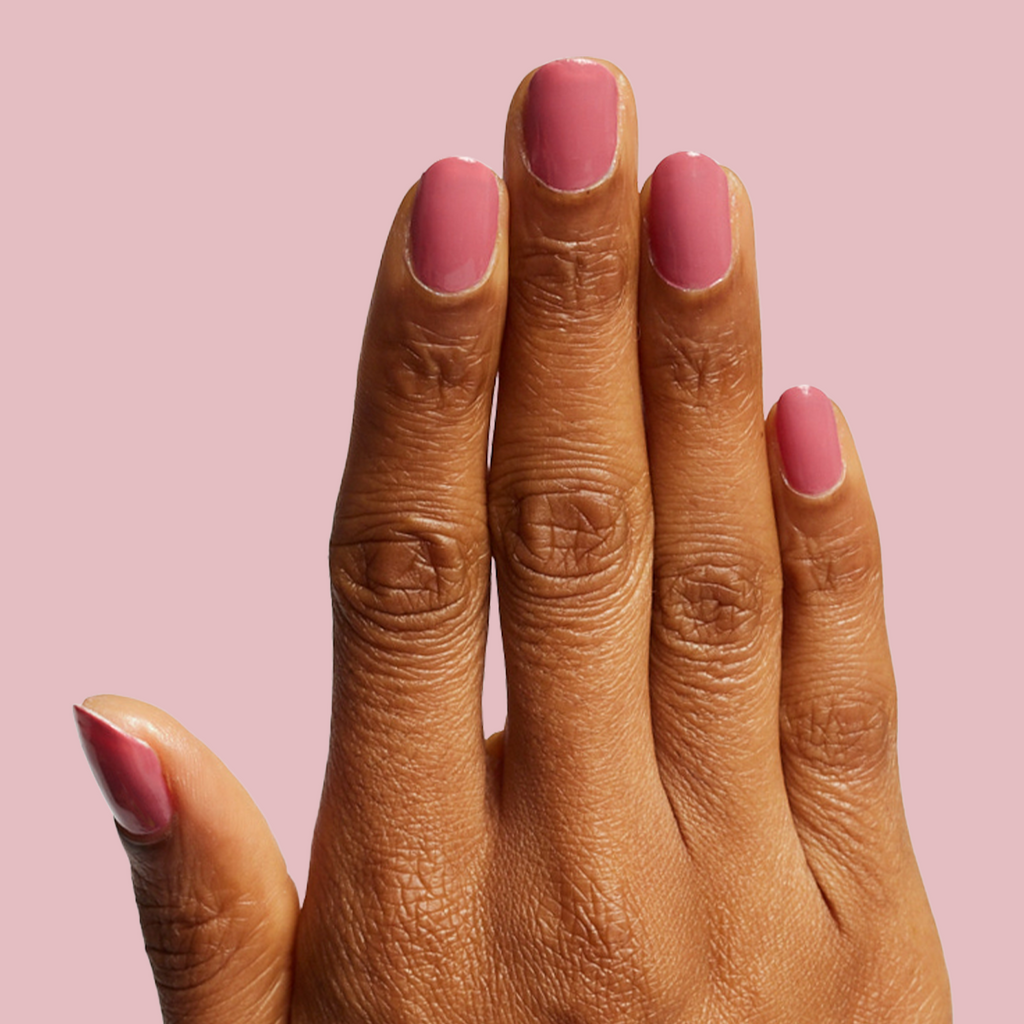 Hand with glossy Primrose polish in warm rosy pink showing a smooth, polished manicure on medium skin tone