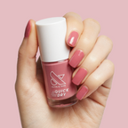 Hand holding Olive and June Primrose quick dry polish bottle with warm rosey pink gel mani visible