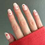 Hand wearing Red Hearts | Short | Round - Tab Press-On nails with neutral base and tiny red heart accents against gray background