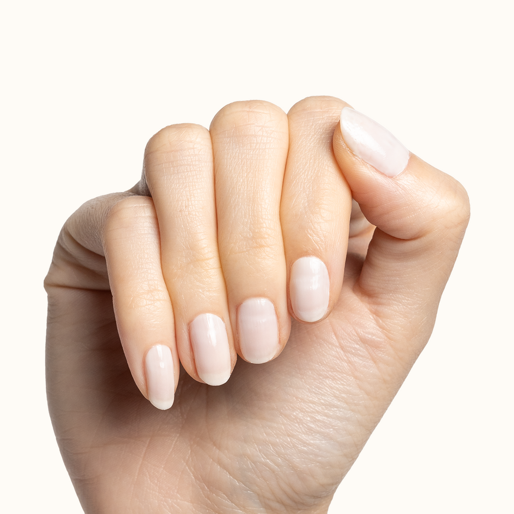 Hand with short natural nails coated in Buttercream sheer milky white polish for a soft manicure look