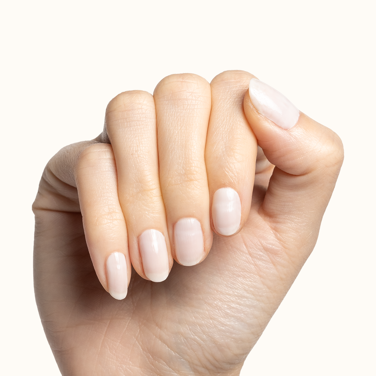 Hand with short natural nails coated in Buttercream sheer milky white polish for a soft manicure look