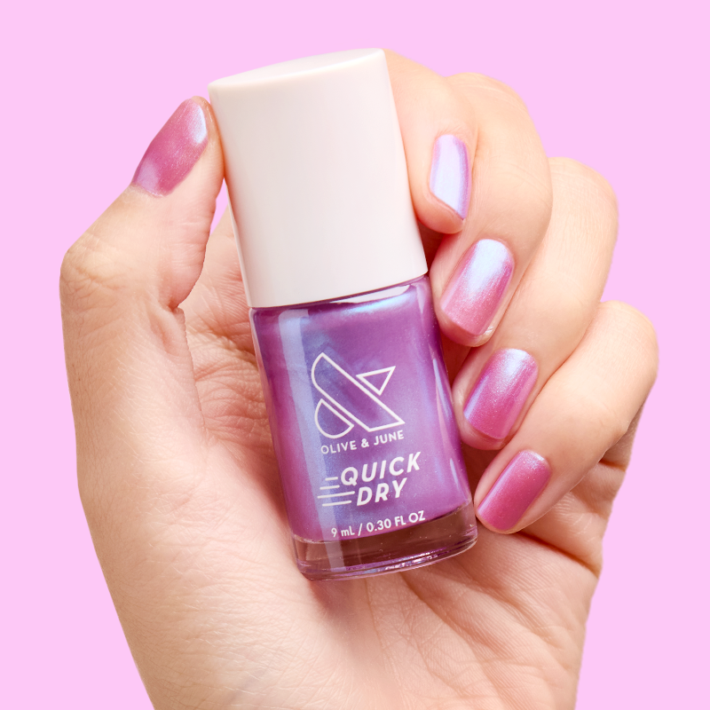 Hand holding Olive and June SWAK quick dry polish bottle with iridescent purple-blue manicure on nails