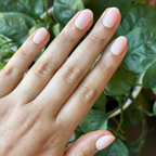 Sandy Shimmer - Press-On | Extra Short | Round neutral sandy beige shimmer press-on nails on a hand with green leaves background