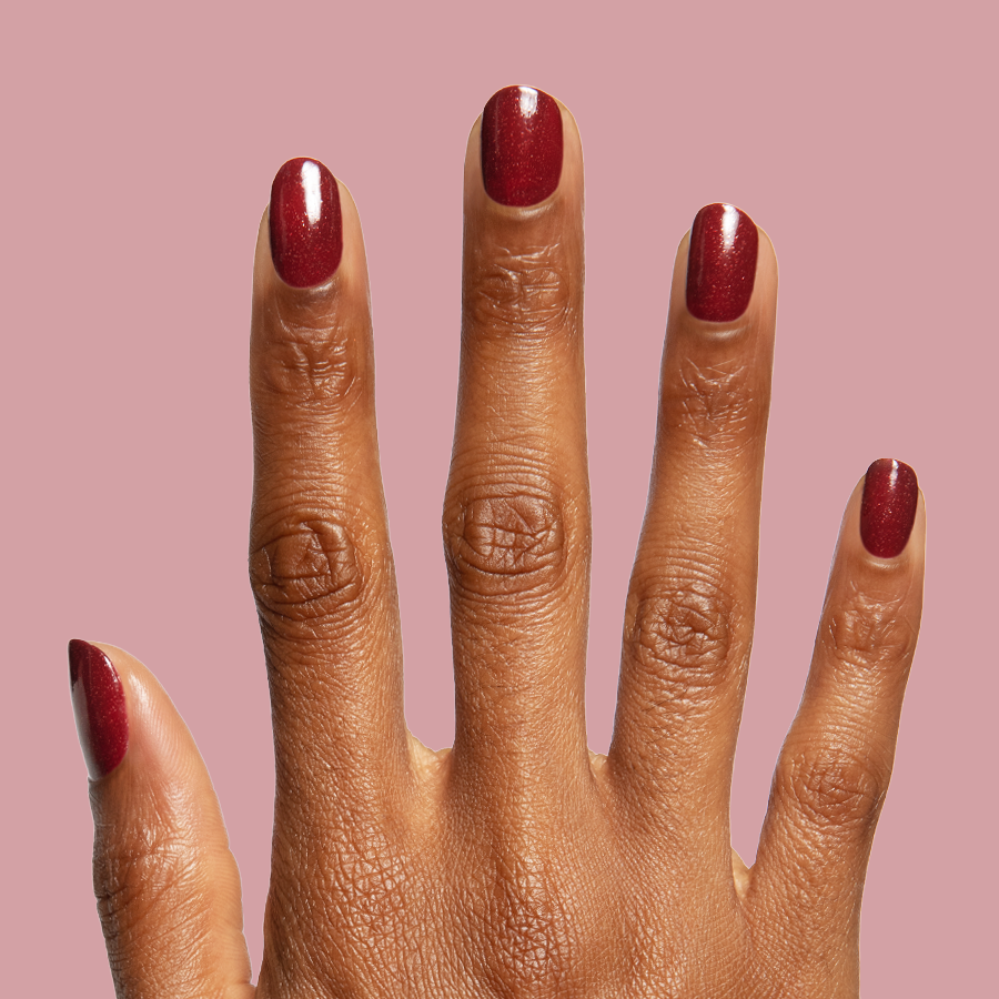 Saucy deep red quick dry polish with subtle shimmer shown on hand against muted rose background