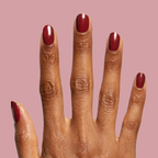 Saucy deep red quick dry polish with subtle shimmer shown on hand against muted rose background