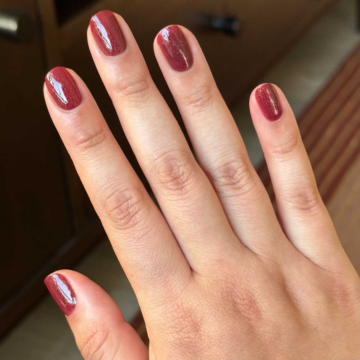 Saucy deep red quick dry gel polish shown on natural short nails with soft indoor lighting background