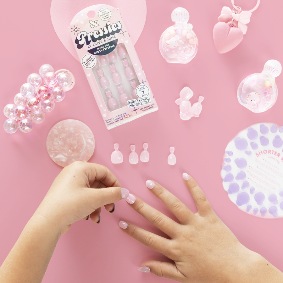Shiny Pink Has My Heart - Pressies | Extra Short Short | Round showing hands applying soft pink false nails on pink surface with mani tools