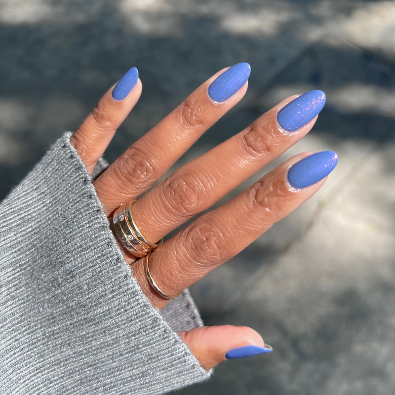 The Sparkle Fairy Effect Top Coat adding subtle iridescent shimmer on matte periwinkle almond-shaped nails for a chic mani