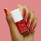 Hand holding Splash of Cran nail polish bottle with shimmery bubbly pinky-red mani on short nails against pink background