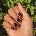 Hand with Stargaze manicure in glossy black polish with delicate rainbow glitter on short natural nails outdoors