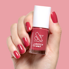 Hand with natural nails painted in bold pinky red Roar quick dry gel polish holding bottle against matching background