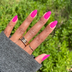 Hand with long almond-shaped nails painted in bright orchid magenta Wildest gel polish against green outdoor background