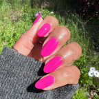 Hand showing glossy bright orchid magenta Wildest gel polish on medium-length nails outdoors with greenery background