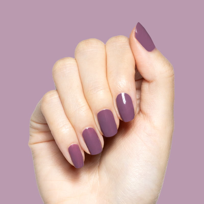 Hand with smooth quick-dry gel polish manicure in Cardigan’s cozy mauve shade on medium-length nails against mauve background