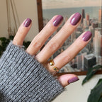 Hand with glossy Cardigan gel polish manicure in cozy mauve shade on natural nails against cityscape background