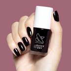 Hand holding Olive and June Covet quick-dry gel polish bottle with matching dark plum manicure on short nails