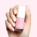 Hand holding Crown nail polish bottle with shimmery princess pink gel polish and matching manicure against light background
