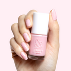 Hand holding Crown nail polish bottle with shimmery princess pink gel polish and matching manicure against light background