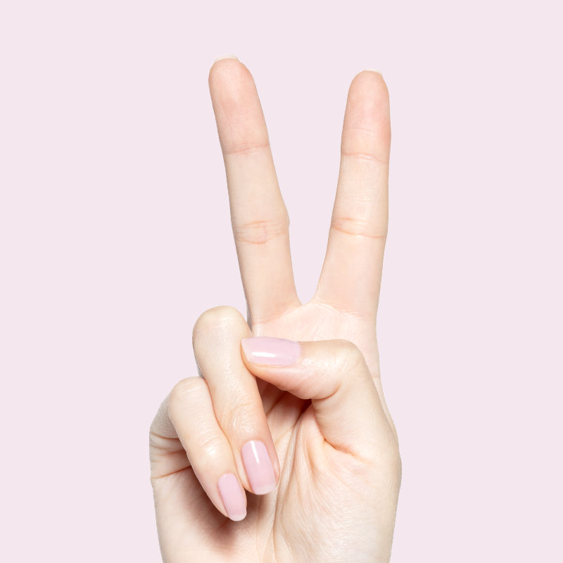 Hand showing peace sign with Glossed sheer lavender-pink gel polish manicure on natural nails against pale pink background