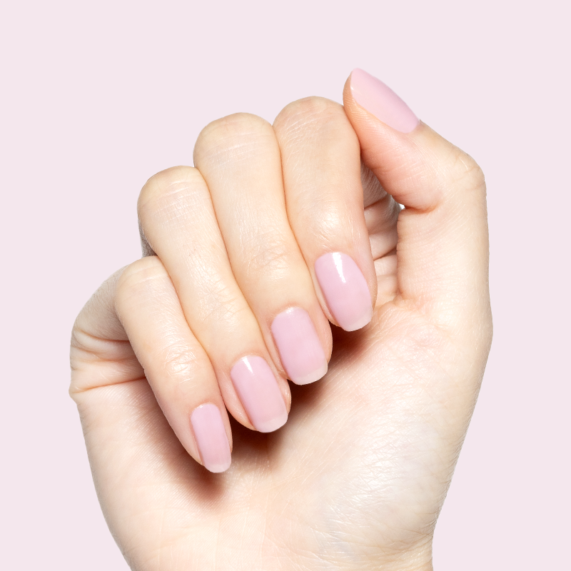 Hand with Glossed sheer lavender-pink gel polish manicure in glossy finish on natural nails against pale pink background