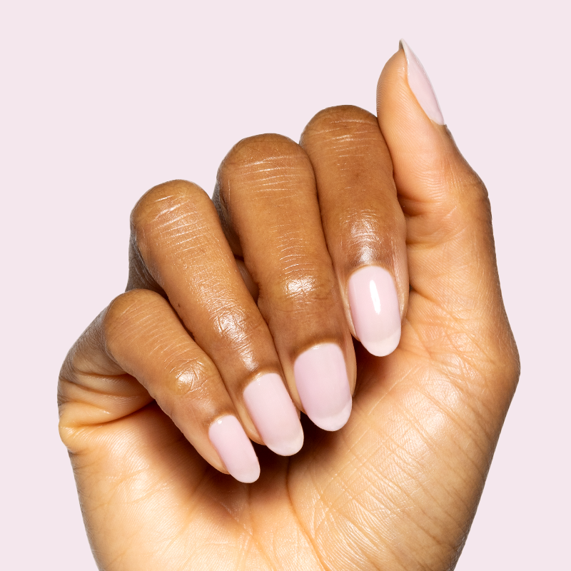 Hand with Glossed sheer lavender-pink gel polish manicure on natural nails against soft light pink background