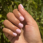 Hand with Glossed quick dry gel polish manicure in sheer lavender-pink shade outdoors with greenery background