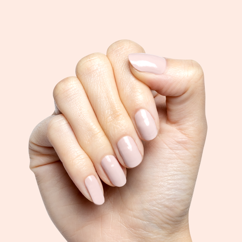Hand with short nails painted in Kitten neutral greige polish showing a clean, polished at home manicure look