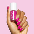 Hand holding Leotard nail polish bottle with matching glossy magenta pink manicure on light pink background