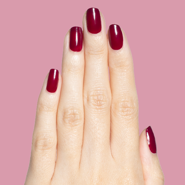 Hand with deep mulberry Mulberry gel polish manicure on natural nails against soft pink background